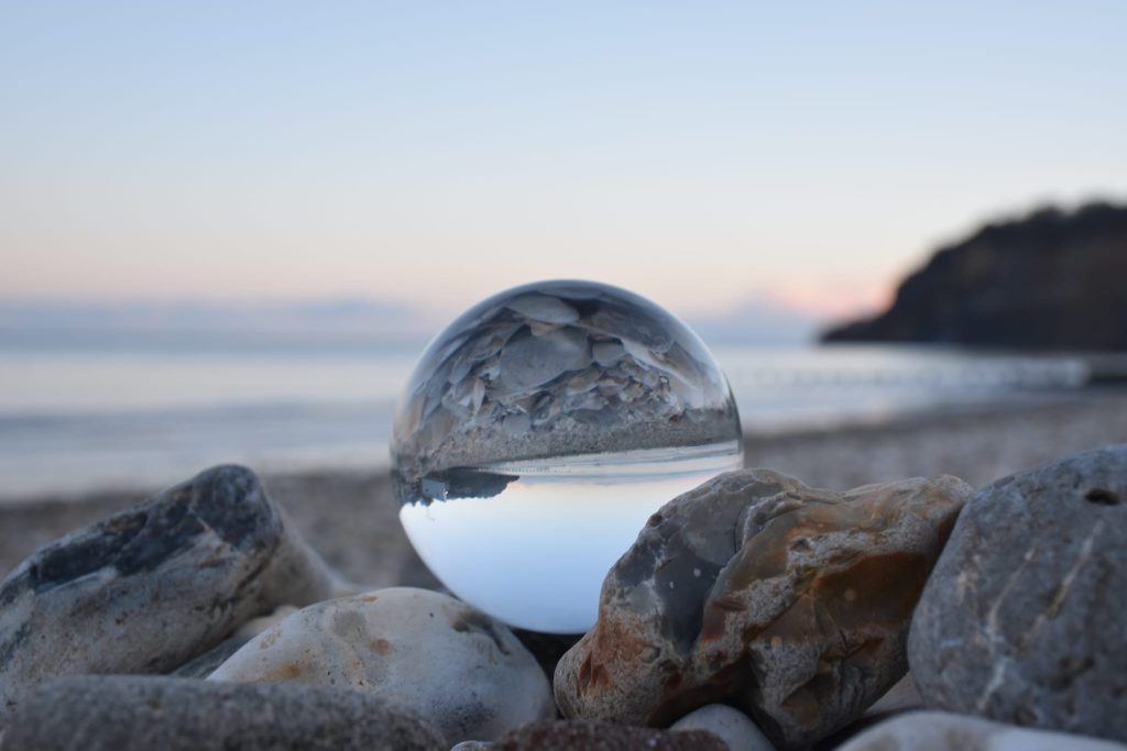 Glass ball at beach, balanced on the rocks. Sunset sky.