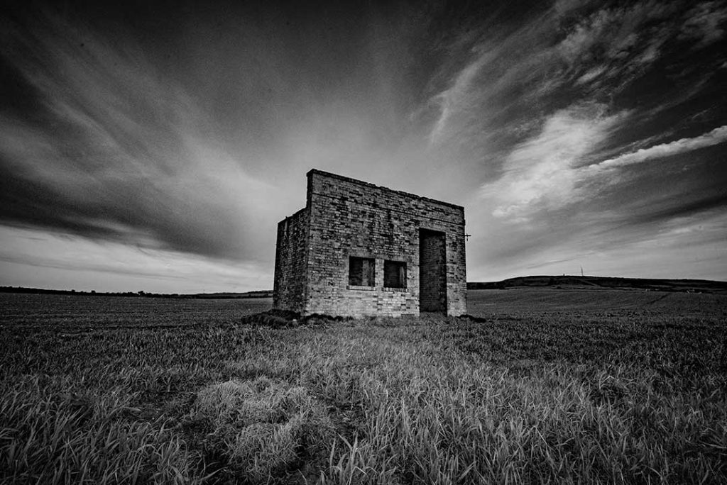 Black and white of a brick shelter against a dramatic grey sky