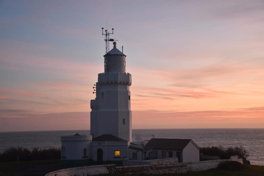 Dusk photo of a historic lighthouse. A white building against a pink and blue sky