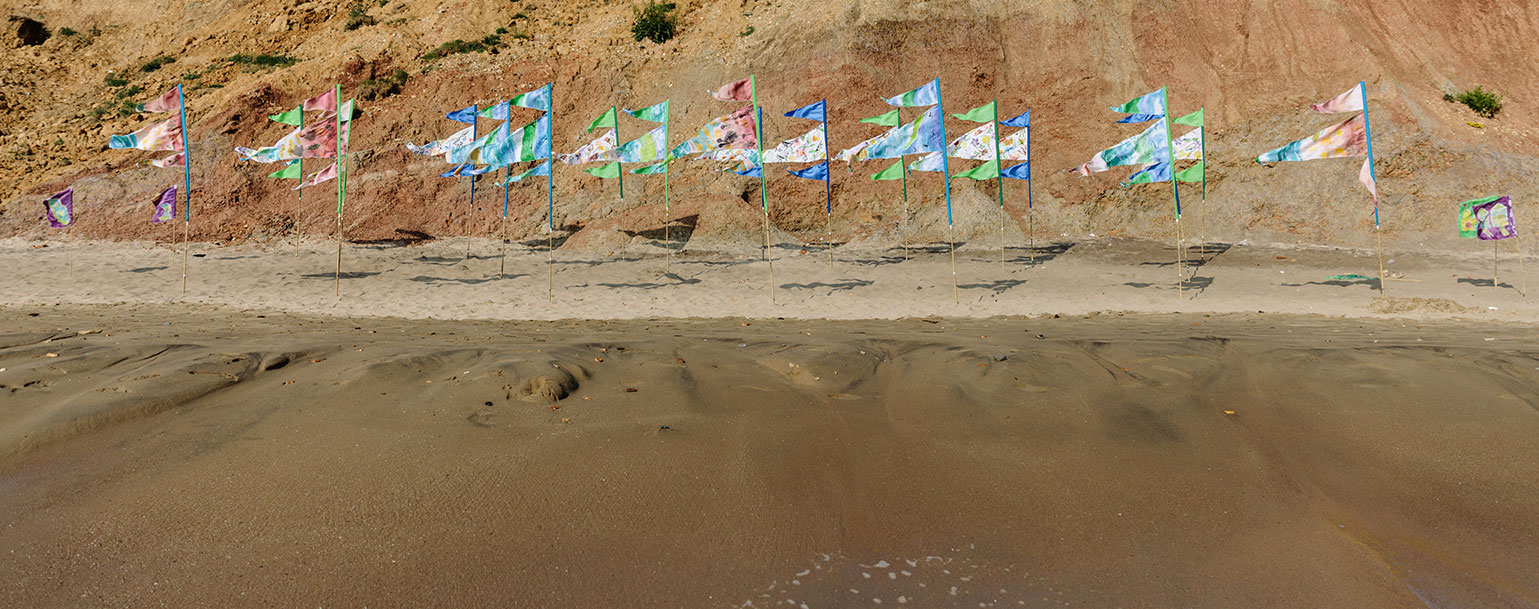 Colourful flags on the beach blowing in the wind on a sunny, sandy beach against the cliff