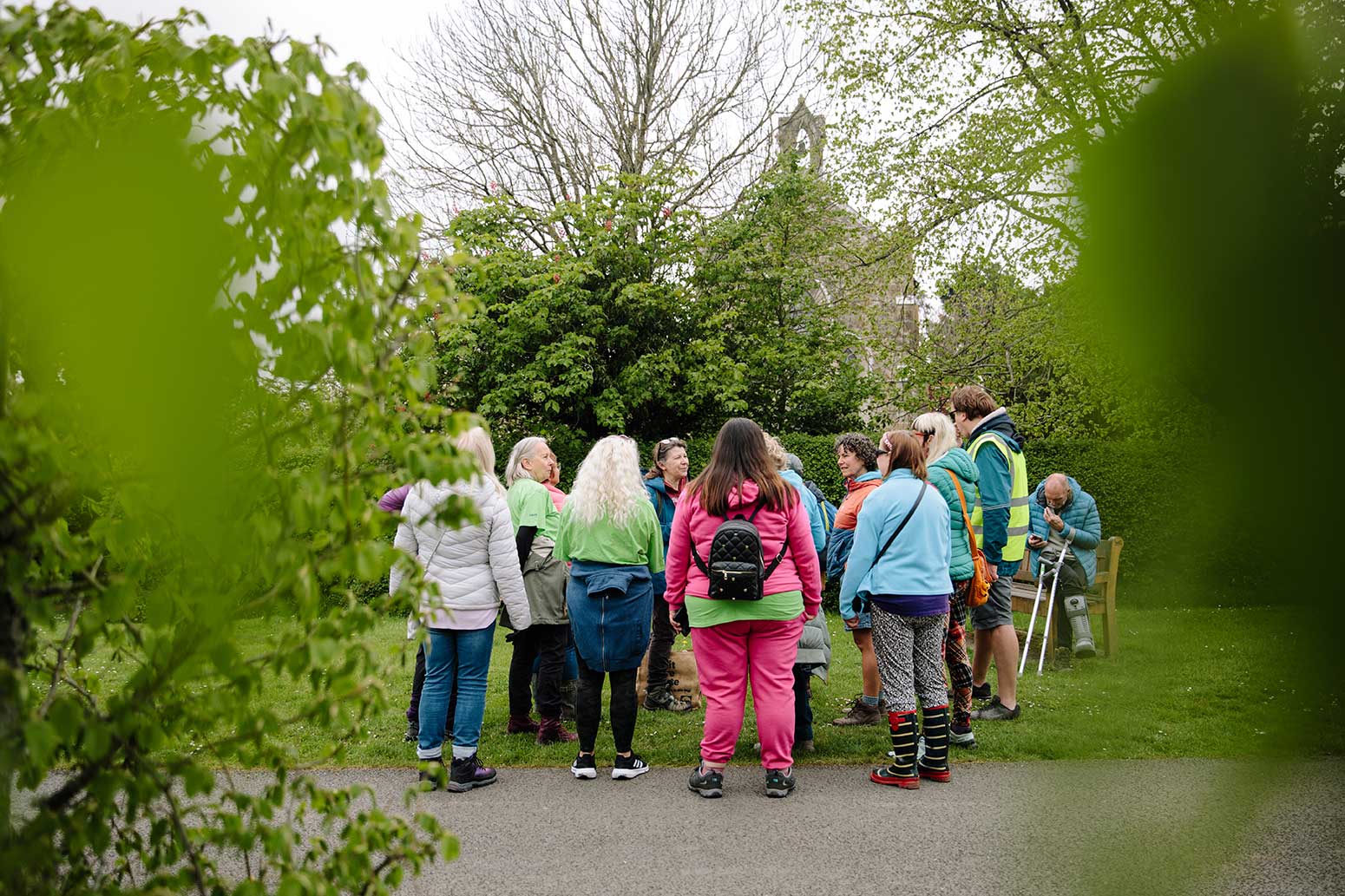 Photo of group of walkers in rural village from behind trees with blurred green leaves either side