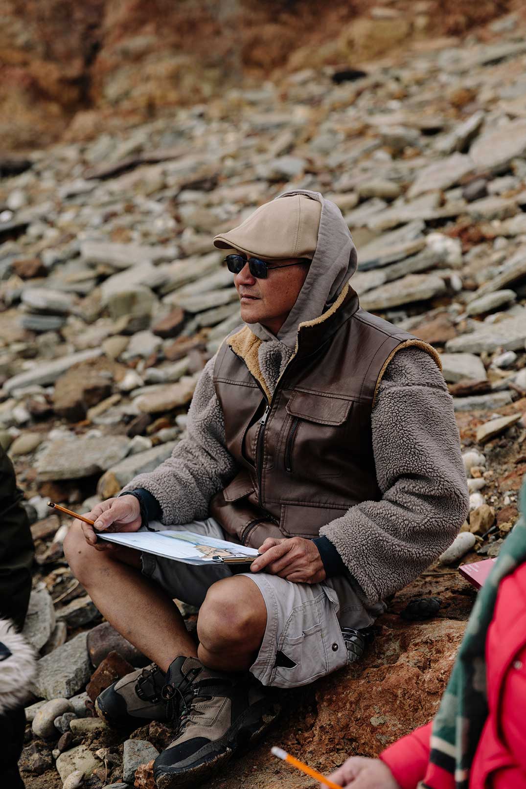 Man sat in shorts and warm clothes looking out to sea sketching the beach with soft focus rocks and stones in the background