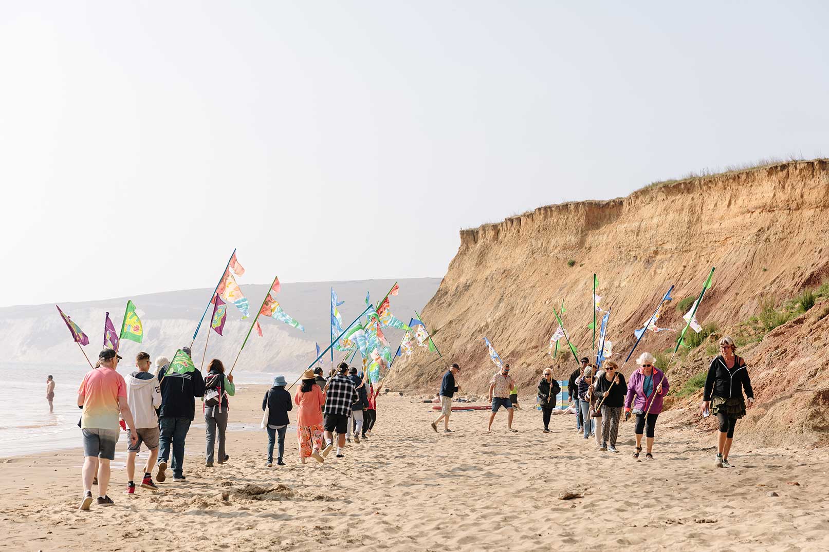 Walks on a flag procession putting colourful flag poles into the ground with sandstone cliff in the background on sunny day