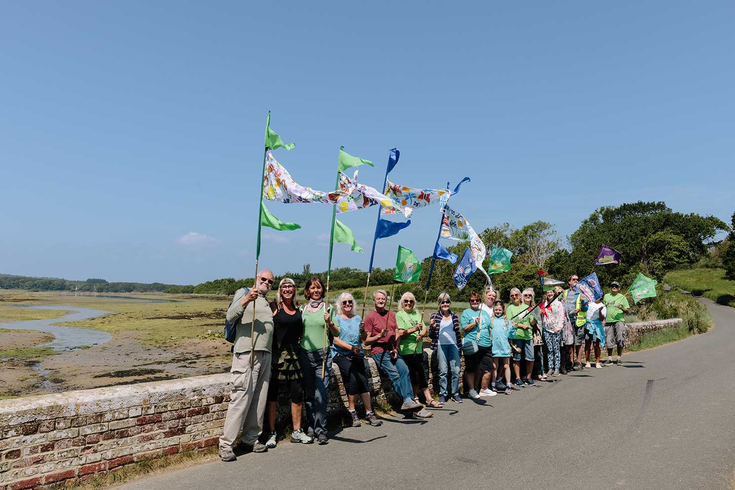 Community group in colourful flag procession stopped by causeway wall for a photo on a bright sunny day