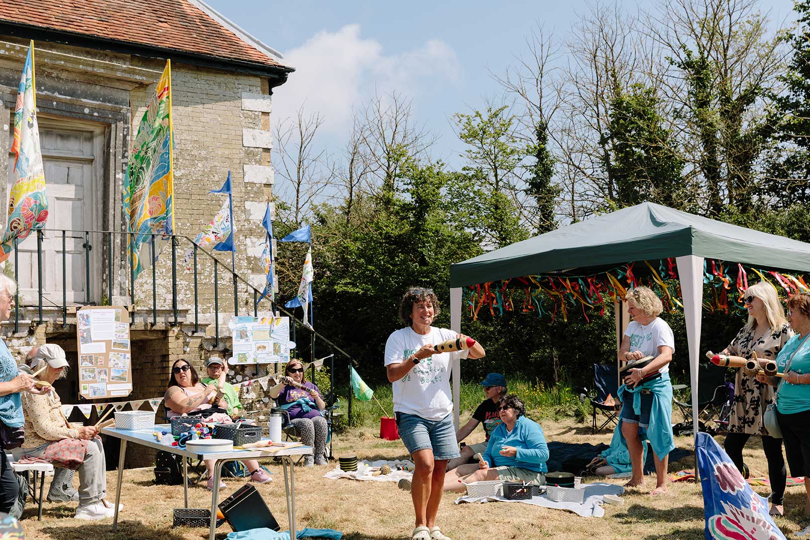 Drumming workshop for adults with learning impairments in a sunny field with historic building behind