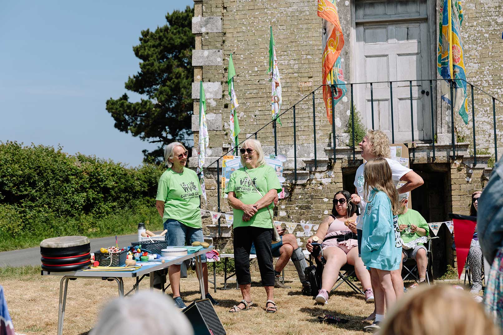 Carnival club organisers talking at outdoor event with historical building and colourful flags behind