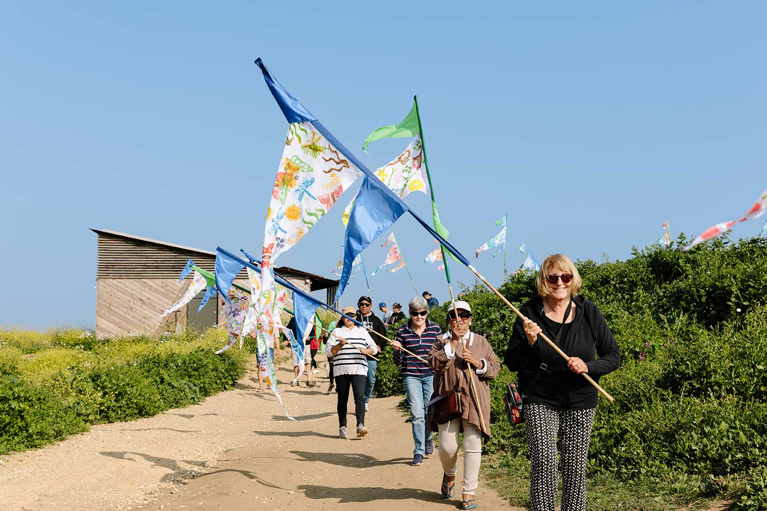 Group of walkers walking along coastal path carrying hand painted flags in sunshine