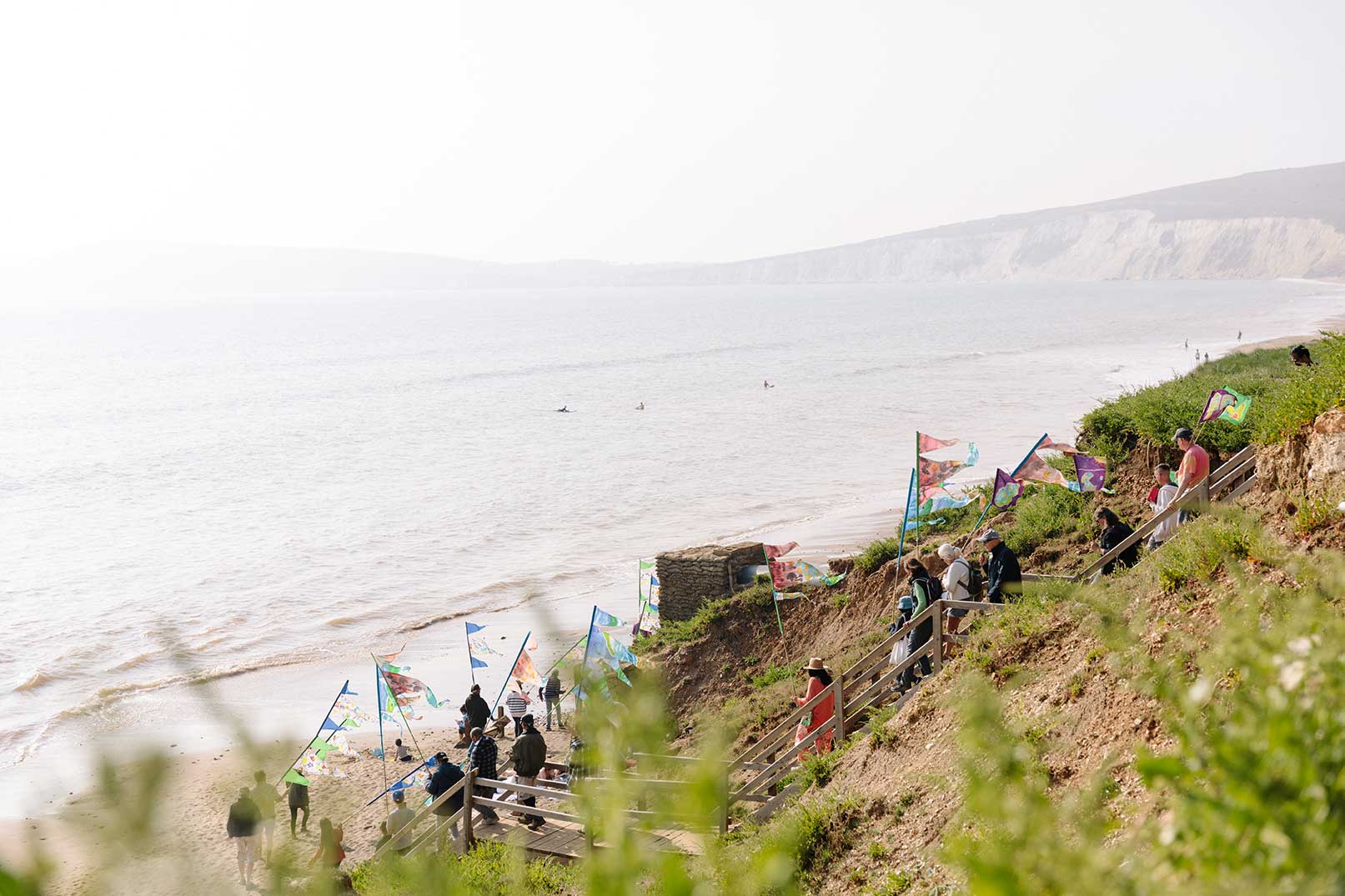 Group of walkers walking down wooden steps onto windy beach carrying hand painted flags