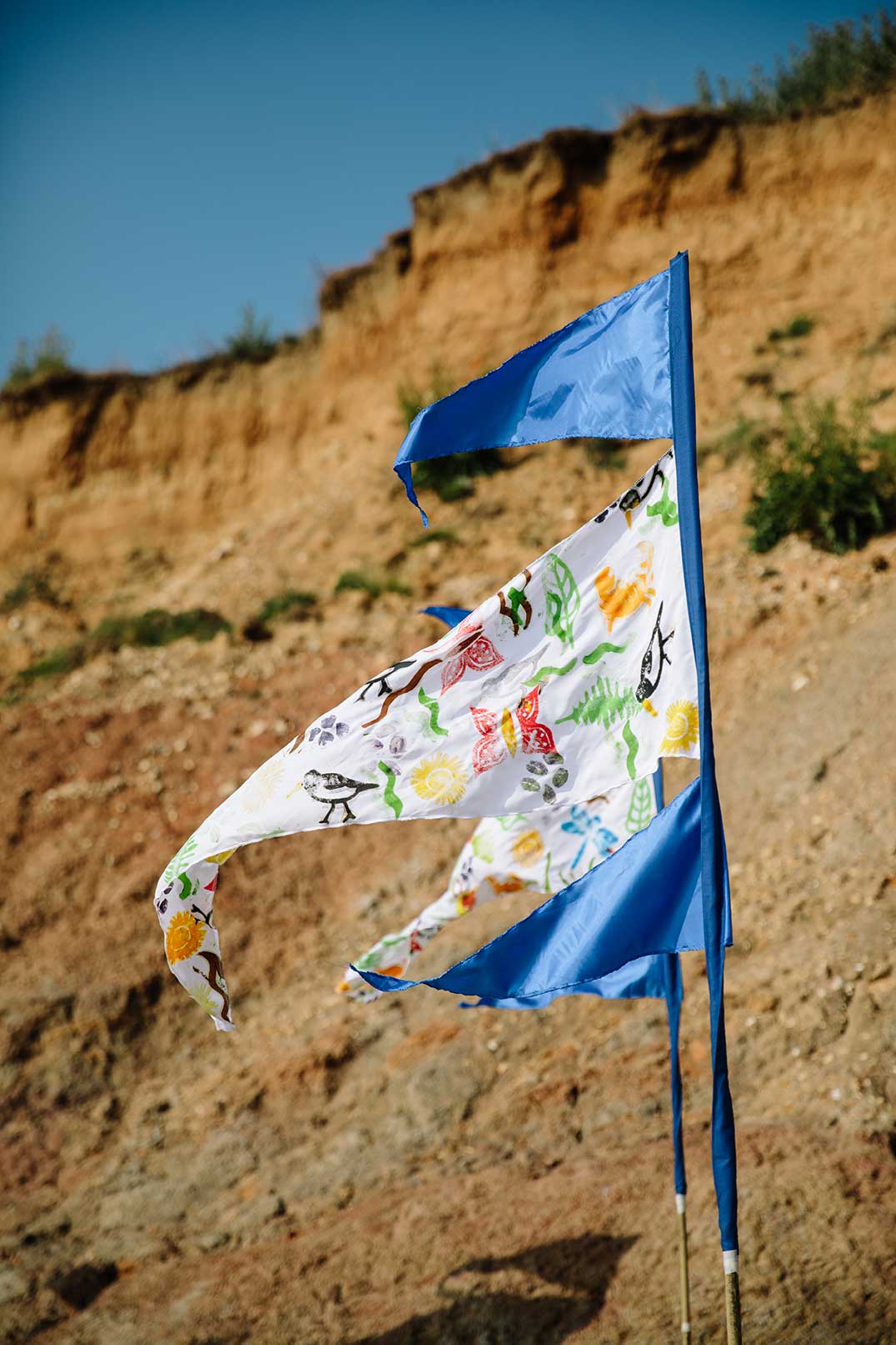 Close up of hand drawn and painted pennant flags blowing in the wind on a beach with warm orange cliffs in the background