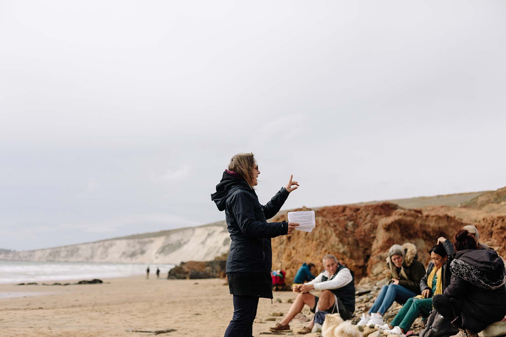 Artist leading mindful session on the beach of group, chalk cliffs in the background