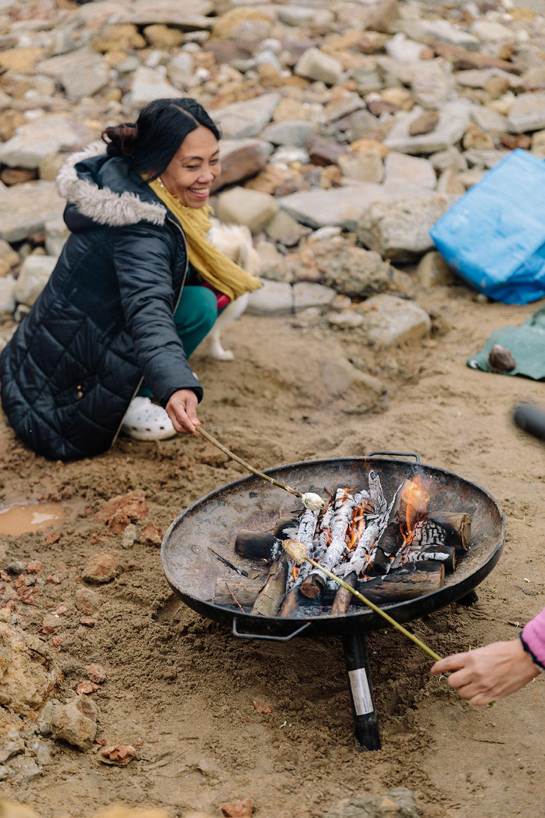 Woman in winter coat toasting marsh mellow over firepit on the beach