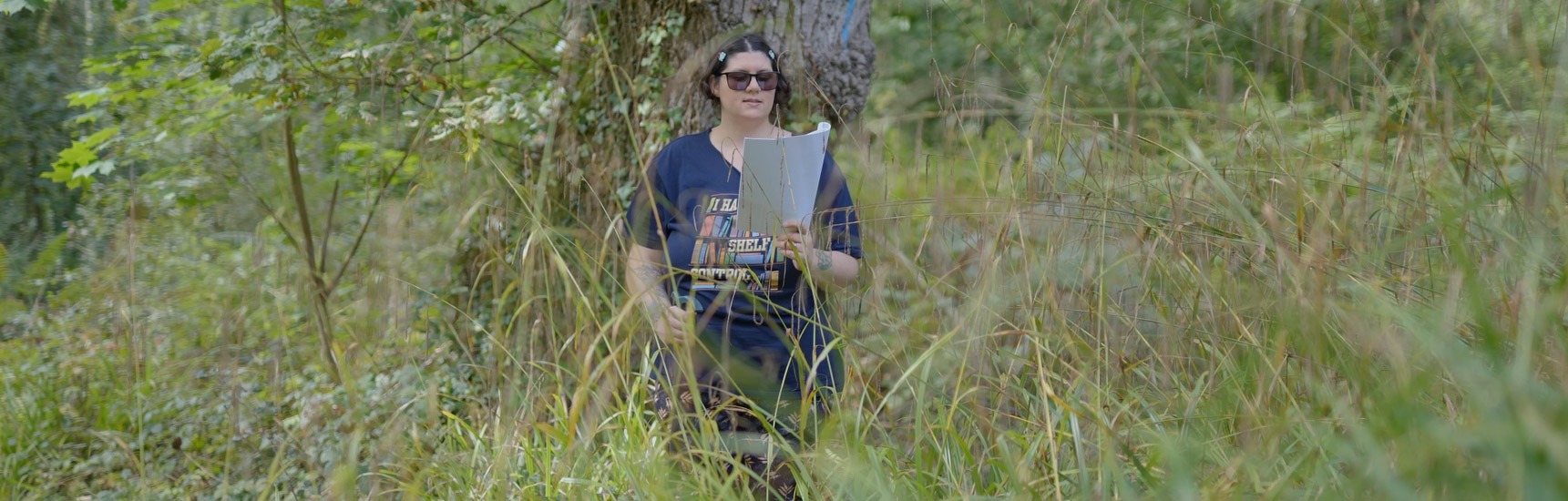 Writer in forest reading from printed paper surrounded by golden grass