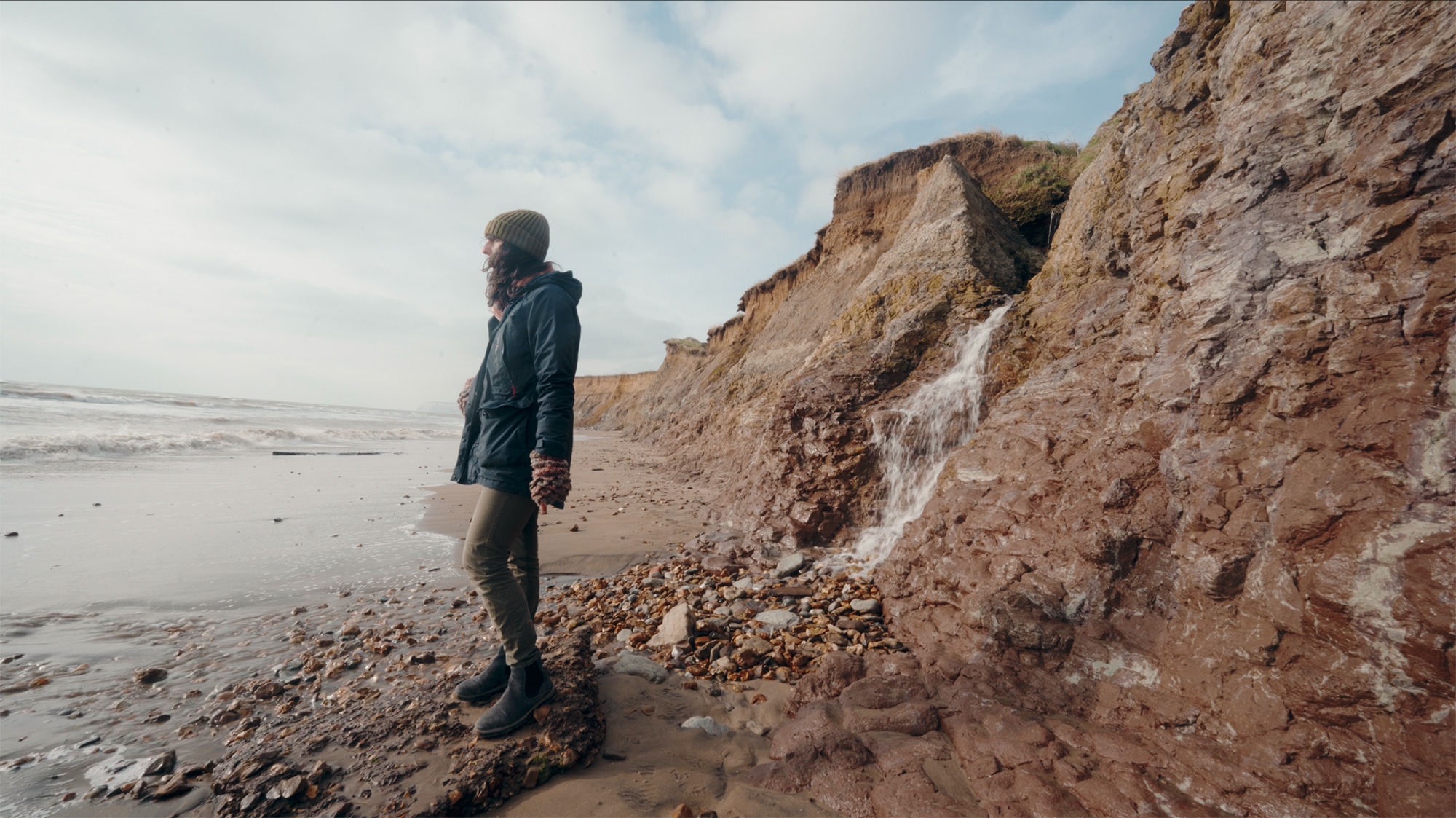 Photo of artist in warm clothes on a wild beach looking out to sea
