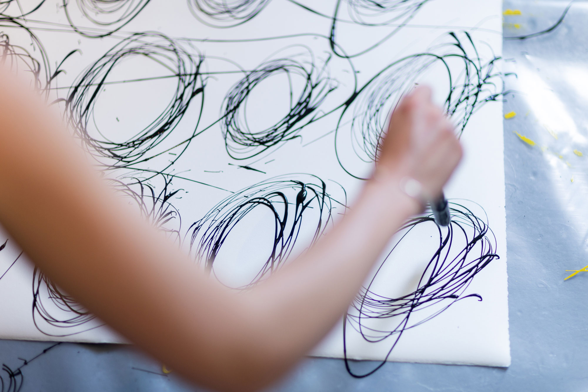 Paintings of lose ink circle on paper on the floor, artist arm blurred in the foreground