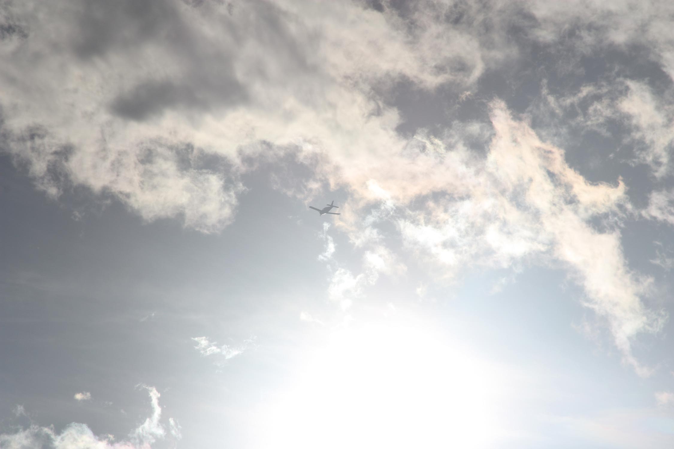 Over exposed photo with blurred sun, fluffy clouds and a plane in the centre of the sky