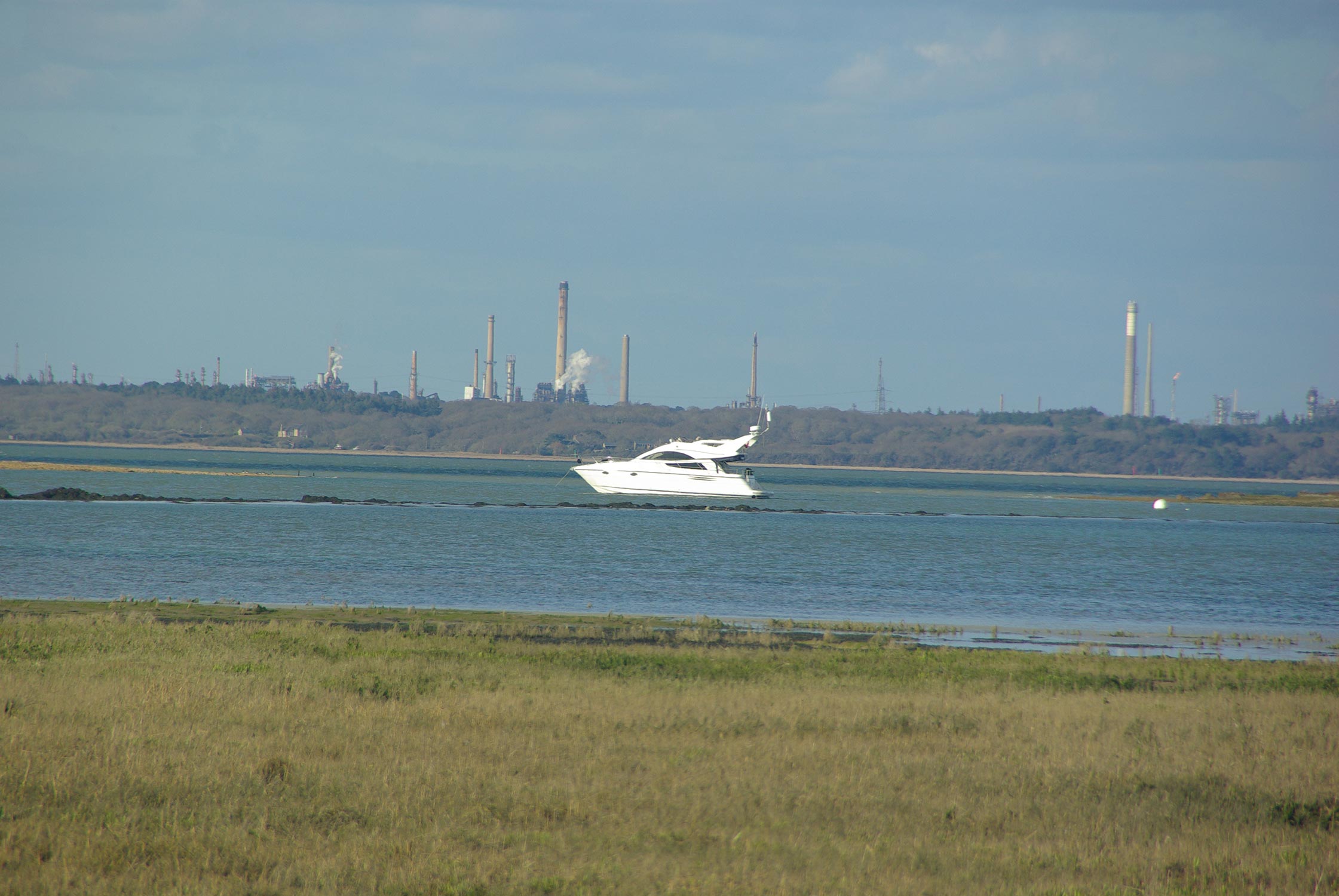 Marsh and grassland with a yacht in the mid ground and factories and Chimneys in background