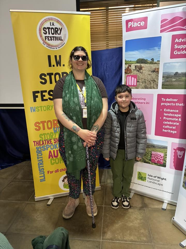 Writer and young performer/writer stood in front of nature and storytelling banners