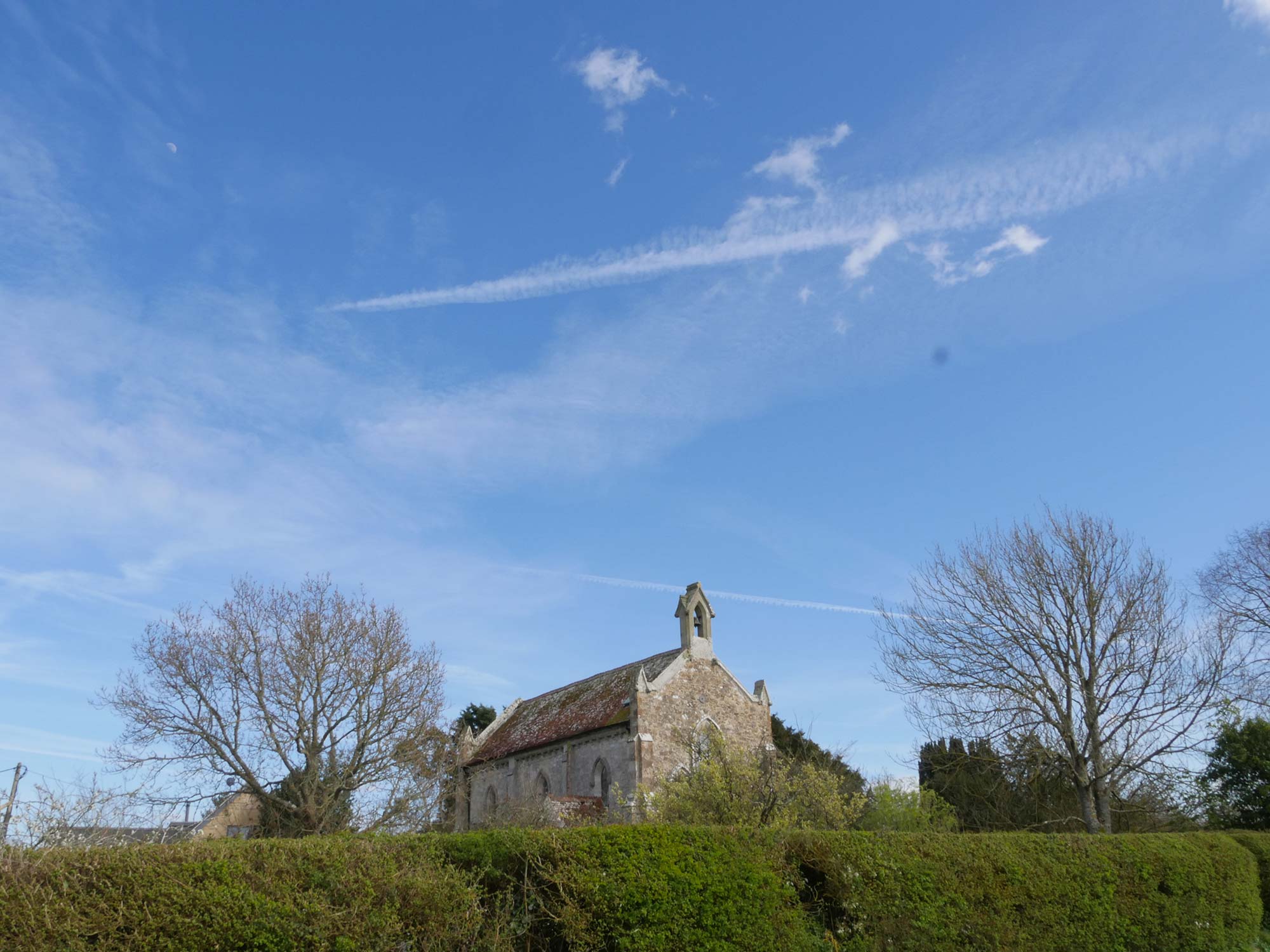 Newtown Church against a blue sky with a thick green hedgerow in the foreground